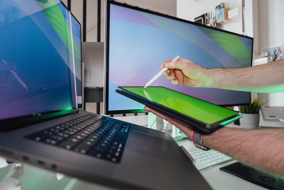 Osoba koristi stylus na tabletu u tehnološkom radnom prostoru s dva monitora